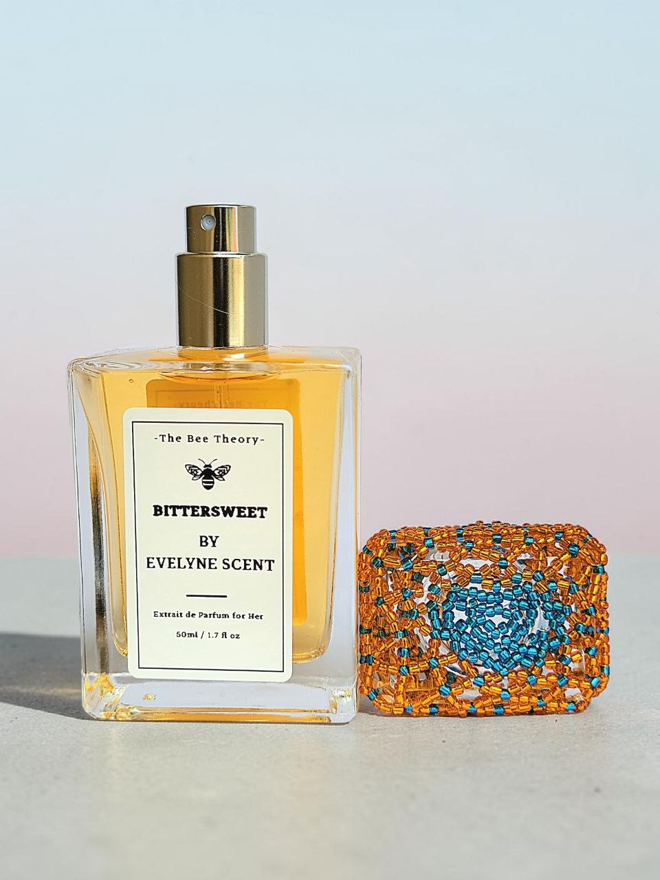 Perfume bottle labeled 'Bittersweet by Evelyne Scent' next to a decorative clutch on a light background